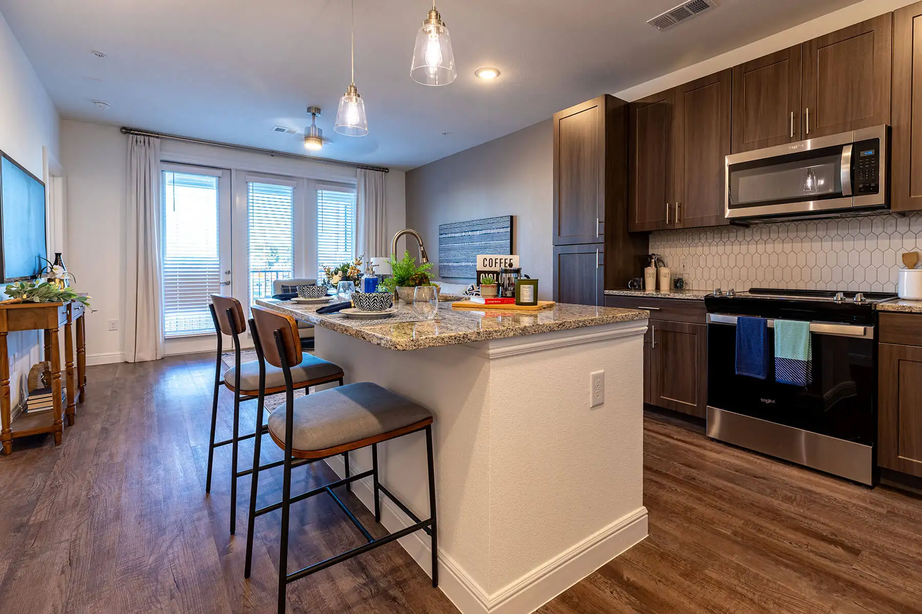 Two chairs pushed up to an island between a living room and kitchen with dark wood cabinets